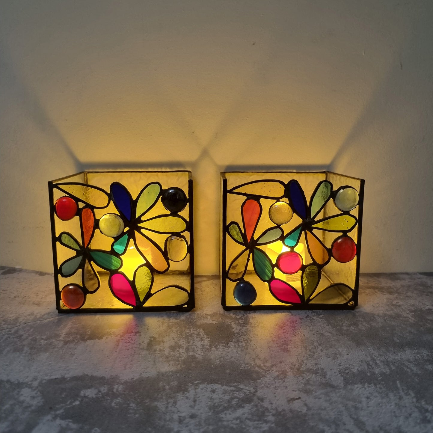 Two colorful stained glass wall lights on a textured surface with a neutral background.