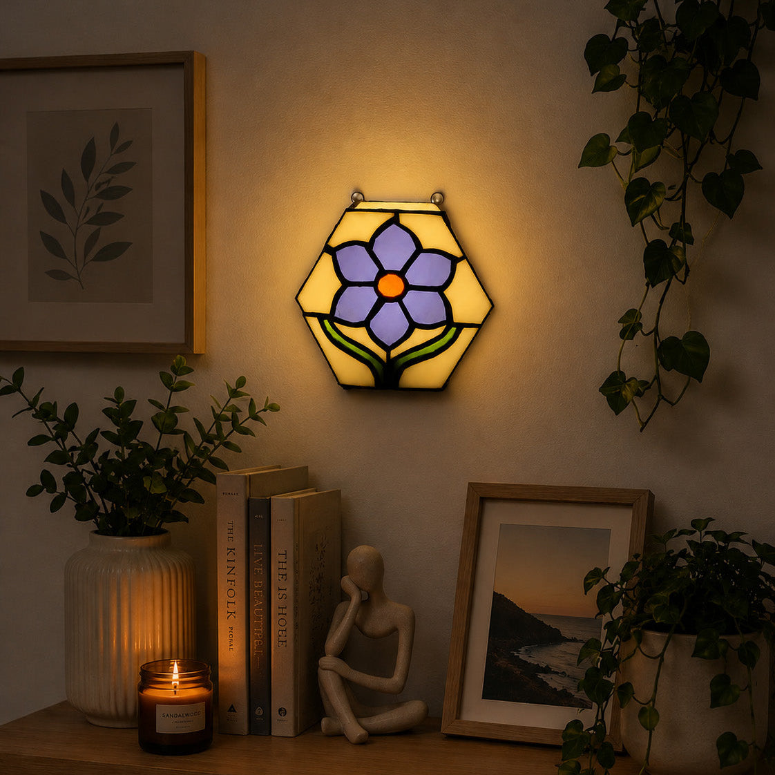 Decorative wall light with stained glass design on a shelf with books, a candle, and plants.