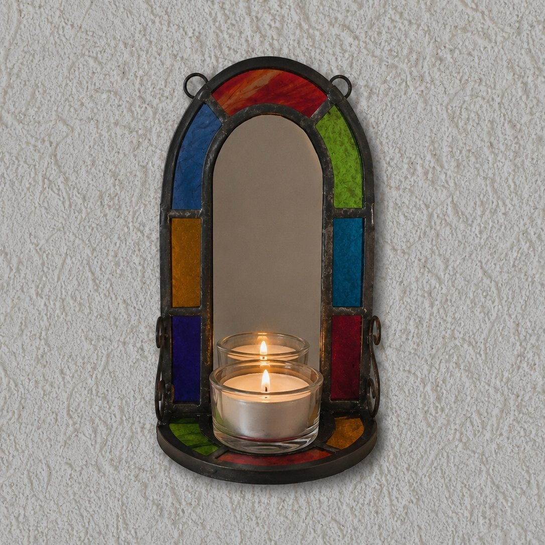 Decorative wall sconce with colorful glass panels holding a lit candle against a plain wall.