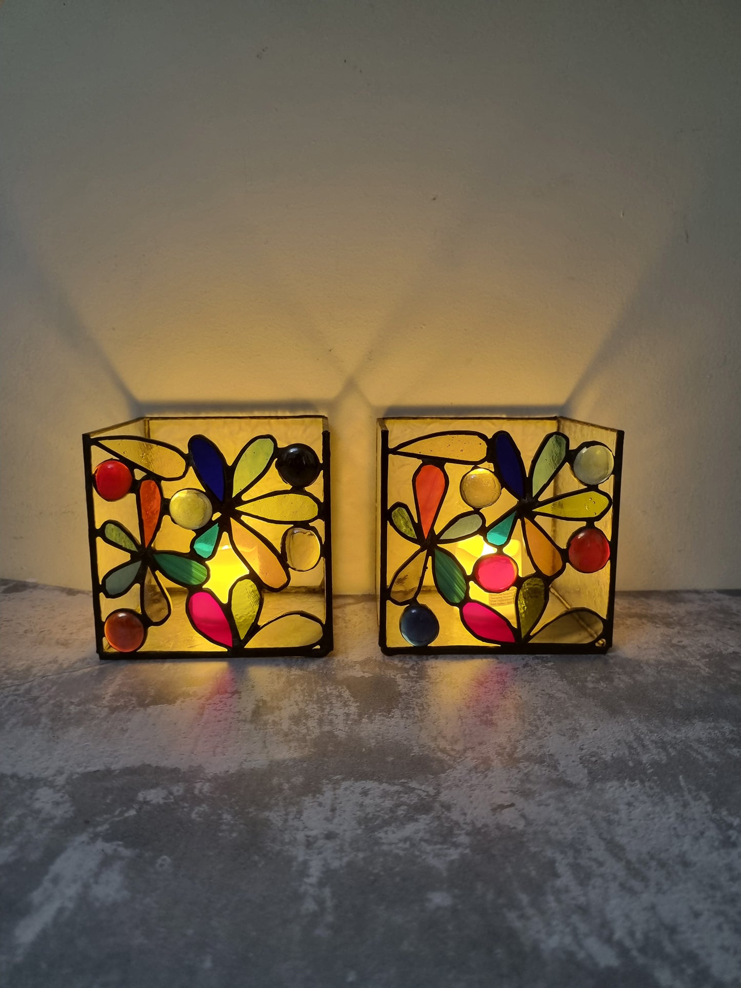 Two colorful stained glass wall lights on a textured surface with a neutral background.