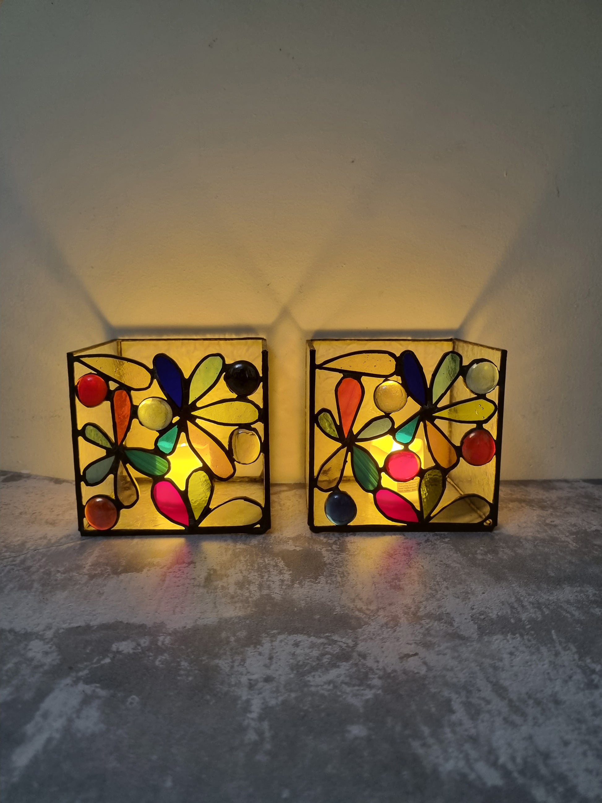 Two colorful stained glass wall lights on a textured surface with a neutral background.