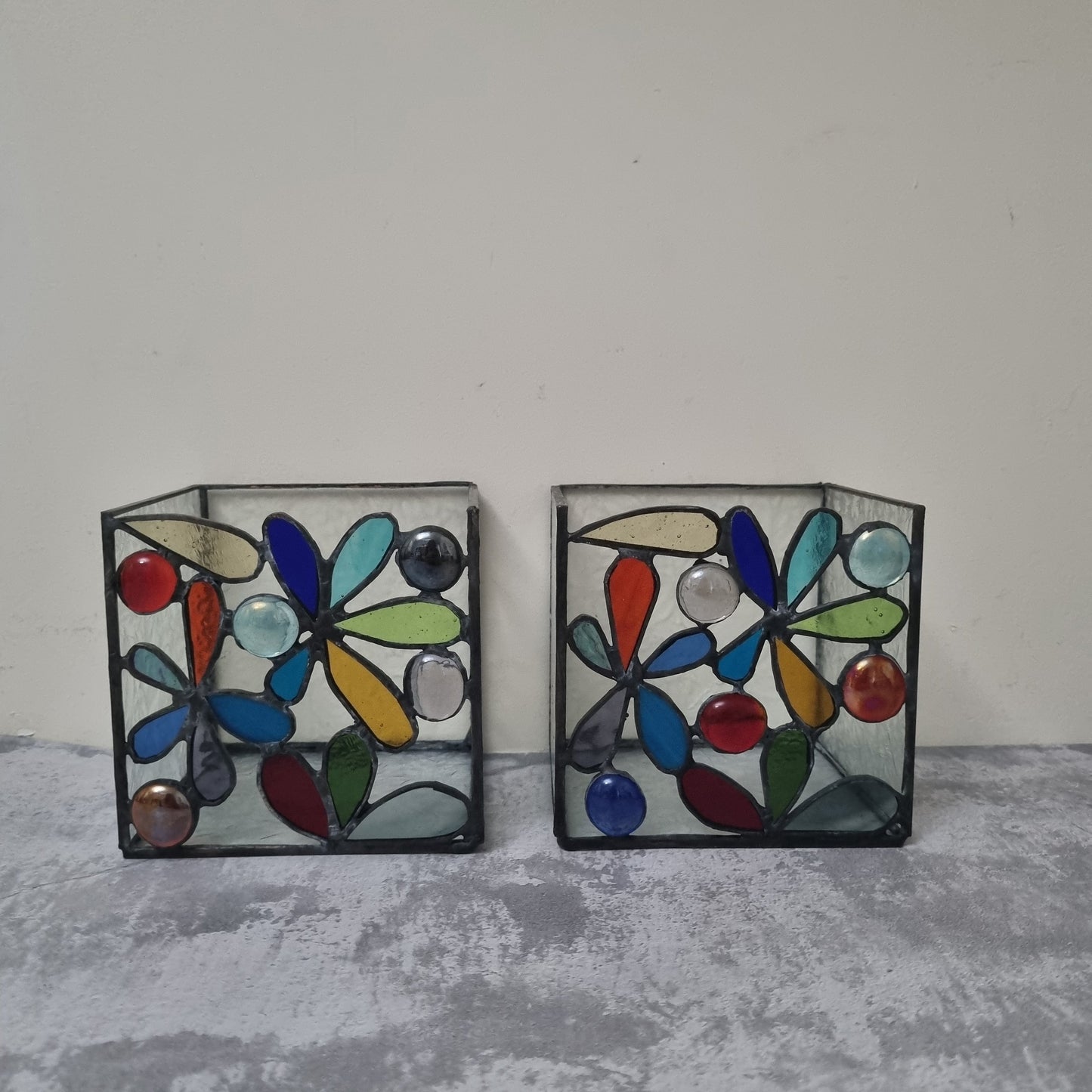 Two colorful stained glass candle holders on a gray surface with a white background