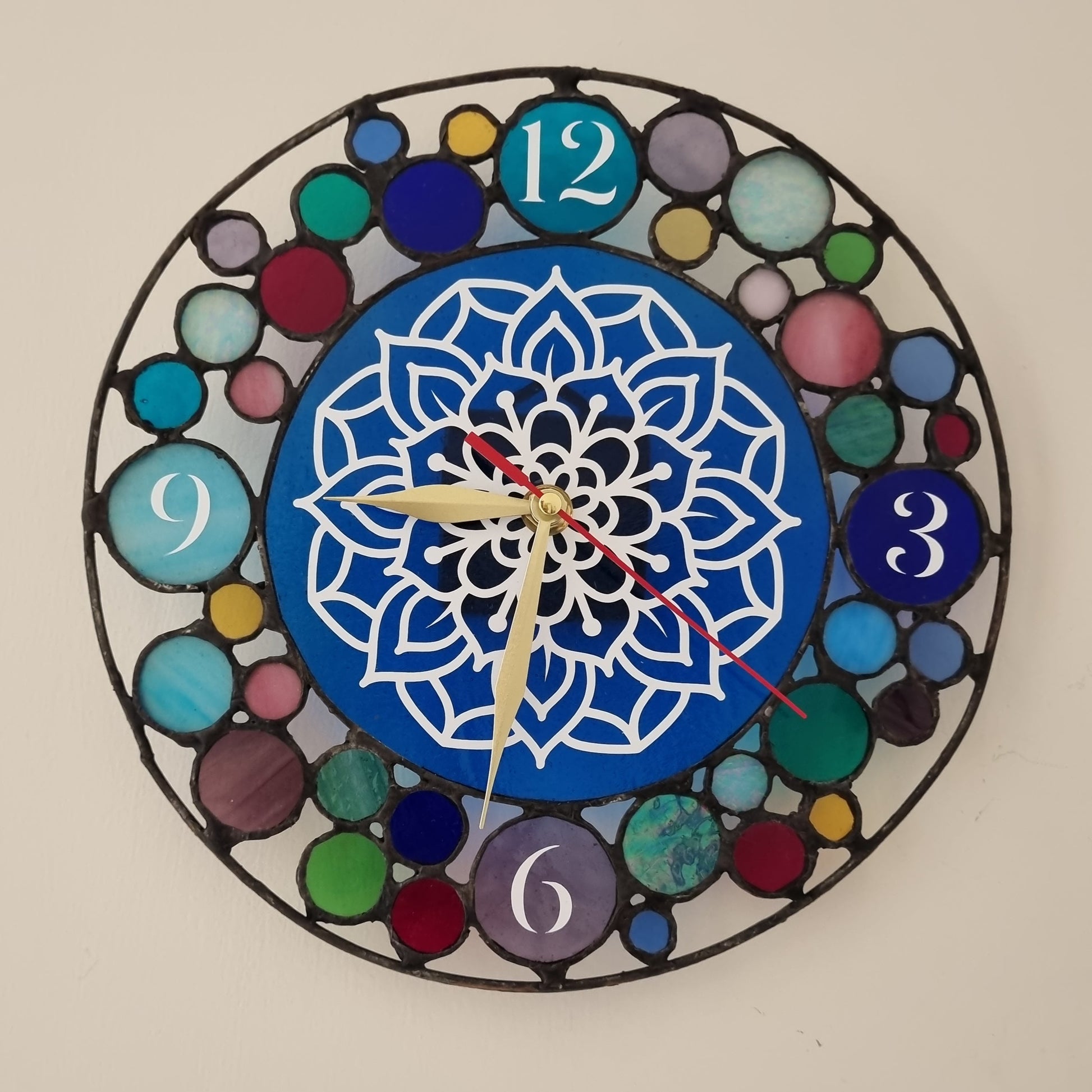 A round glass wall clock with multicolored floral patterns and numbers in a geometric design.